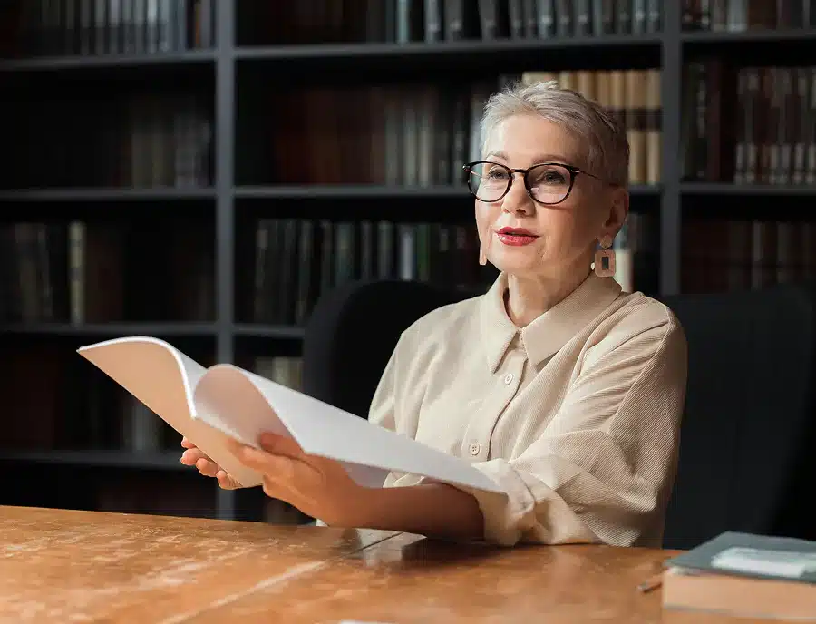 An older woman with glasses is intently reading a book